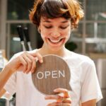Small business owner holding an open sign in her shop window, a brand worth protecting with a trade mark